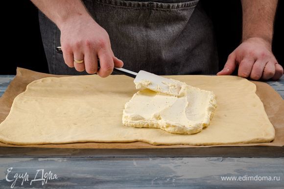 Разделите подошедшее тесто на две части, раскатайте их в прямоугольники и равномерно распределите по всей поверхности теста творожную начинку.