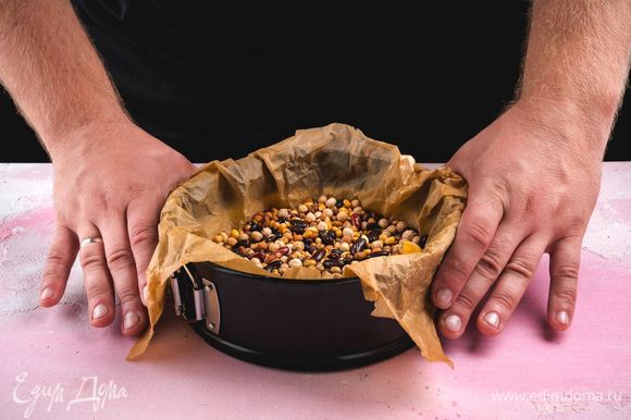 Дно пирога проткните вилкой, выстелите пергаментом и положите слой фасоли, чтобы тесто пропеклось равномерно. Выпекайте основу для киша при 180°С в течение 20 минут.