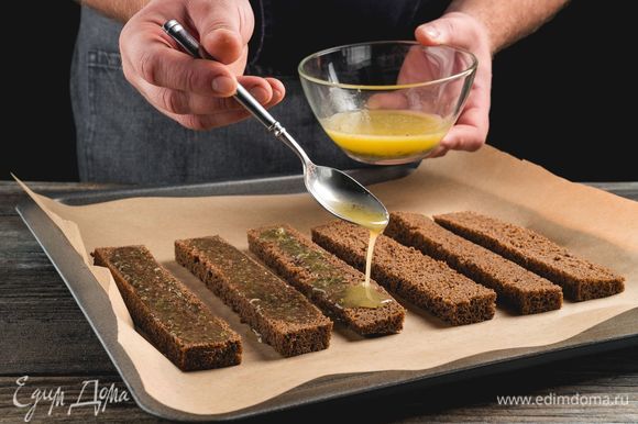 Полейте чесночным маслом с травами кусочки хлеба и выложите на противень с пергаментной бумагой.