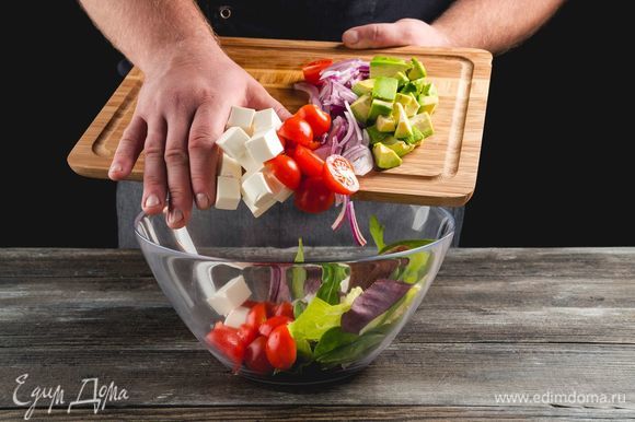 Порвите салатные листья руками и застелите блюдо. Выложите горкой вперемешку авокадо, фету, томаты и красный лук.