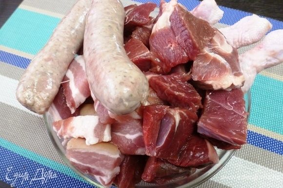 Все виды мяса берем примерно в одинаковых пропорциях. Нарезать все не слишком мелкими кусочками. Куриные голени я оставила как есть. А колбаски нужно разрезать острым ножом на 3–5 частей в зависимости от размера.