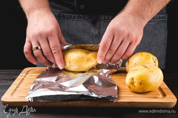 Промойте картофель, плотно оберните фольгой и отправьте выпекаться в разогретую до 180°C духовку на 1 час.