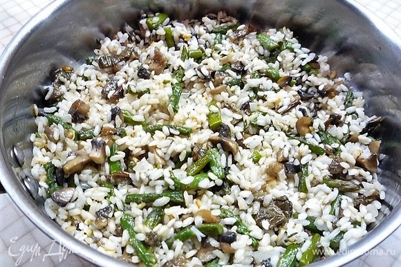 Через 5–7 минут после добавления первой партии бульона в рис, добавляем грибы и спаржу. Аккуратно перемешиваем и доводим до готовности в течение 15 минут, по необходимости добавляем бульон и пробуем рис на готовность.