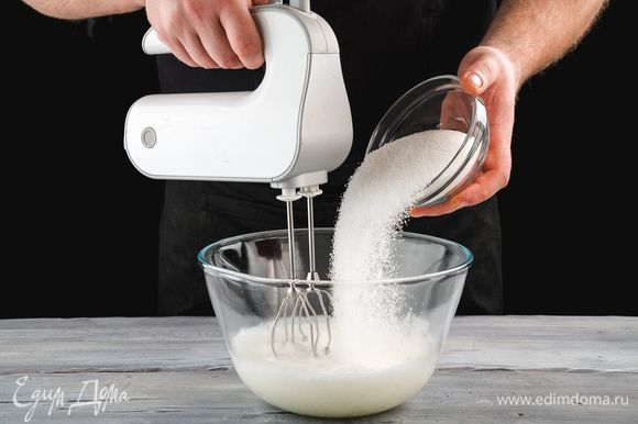 Приготовление пирожных начните с меренги. В чашу поместите яичные белки комнатной температуры и взбейте их миксером до появления мелких пузырьков. Постепенно всыпьте сахар в 3 захода, продолжая взбивать массу. Взбивайте белки до устойчивых пиков.