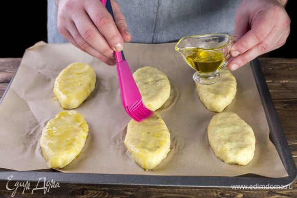 Выложите картофельные зразы на противень, застеленный пергаментом, сверху смажьте зразы маслом.