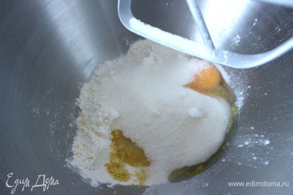 Натереть на мелкой терке цедру 1 лимона. В чашу комбайна поместить часть муки с разрыхлителем (примерно 1/3 часть), всю цедру, 1 яйцо, часть йогурта, сахара, масла, перемешать на небольшой скорости.