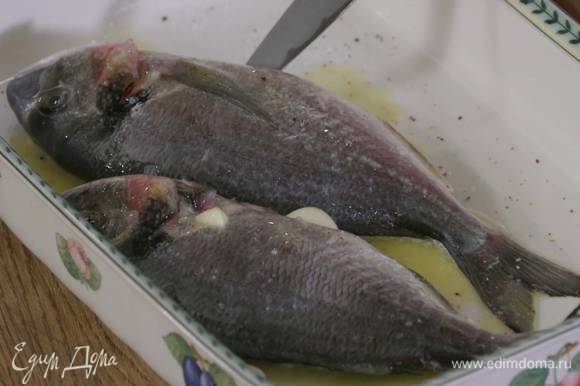 Рыбу выложить в жаропрочную керамическую форму, слегка посолить, поперчить, полить растопленным маслом, а зубчики чеснока поместить в брюшко.