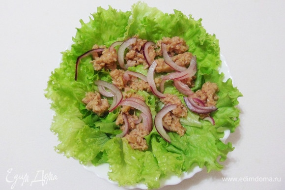 Салатные листья порционно разложить по тарелкам. Сверху положить кусочки консервированного тунца и маринованный лук.