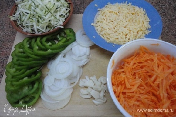 Нарезать лук, перец любого цвета и чеснок тонкими кольцами или пластинками. Морковь, кабачки и сыр натереть на крупной терке. Зелень порубить. Разогреть духовку до 200–220°C.