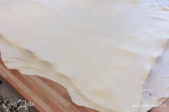 На припыленной мукой поверхности тонко раскатать тесто прямоугольной формы. Полотенце присыпать мукой и аккуратно перенести тесто на полотенце. При переносе тесто нужно осторожно и равномерно растягивать руками.