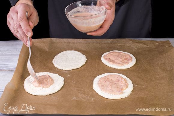 Дрожжевое тесто разморозьте и раскатайте на мини-пиццы. Выложите заготовки на противень, застеленный пергаментной бумагой, и смажьте майонезно-томатным соусом.
