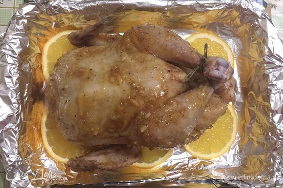 На апельсины выложить курицу и запекать при 190°C 1–1,5 часа (в зависимости от размера курицы), до готовности, часто поливая выделившимся соком.