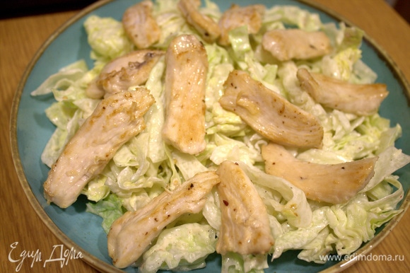 На дно плоской тарелки перенести салат с заправкой, сверху — кусочки курицы.