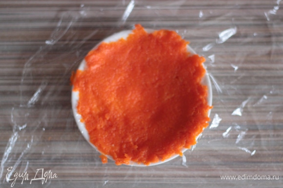 Блюдце застелить кусочком пищевой пленки, аккуратно выложить ложку натертой моркови и разровнять. Стараться, чтобы не было дырочек и получилась как бы тонкая лепешка.