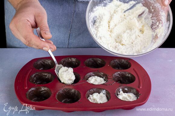 Достаньте формочки с шоколадной основой из морозилки. Каждую из них наполните творожной массой наполовину.