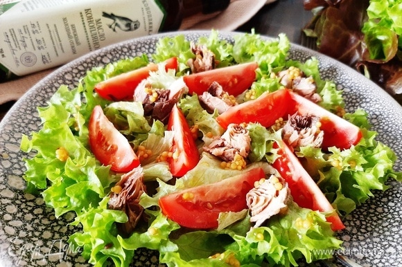 На блюдо выкладываем листья салата, сверху — дольки томата и кусочки тунца. Поливаем заправкой. Подаем салат сразу. Приятного аппетита!
