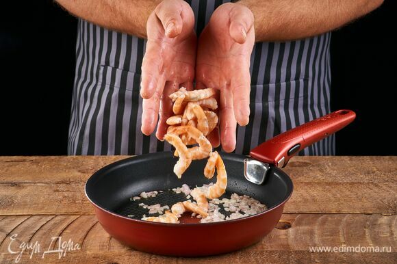 Обжарьте лук на сковороде в небольшом количестве растительного масла. Добавьте очищенные креветки. Обжарьте вместе луком около 2 минут.