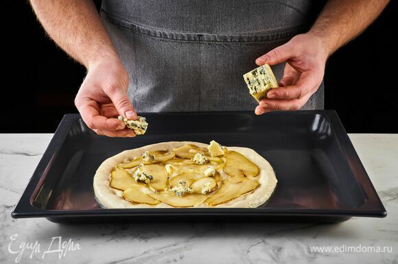 Выложите на тесто карамелизированную грушу. Сверху — кусочки горгонзолы. Выпекайте пиццу в разогретой до 250°C духовке 12–15 минут.