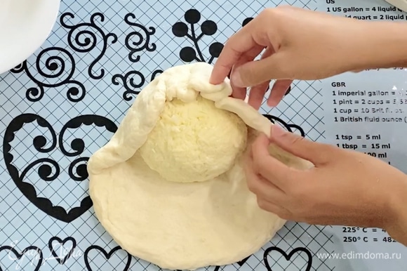 Подошедшее тесто выложить на стол. Руками сформировать небольшой круг-основу для сырного шара. В центр теста выложить сырный шар и собрать тесто вокруг сыра, создавая оболочку сырного шара, защипнуть края теста сверху сырного шара.
