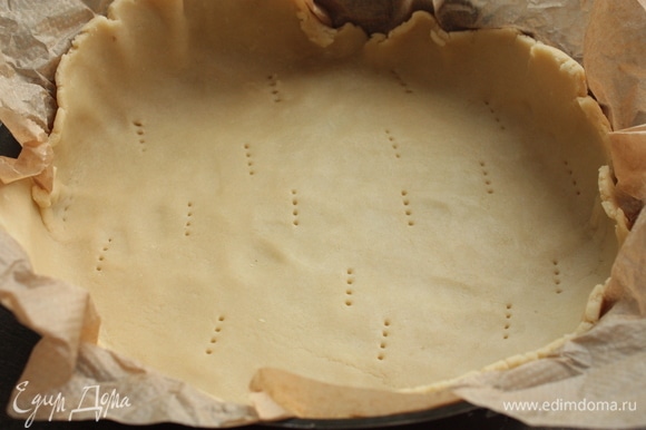 Охлажденное тесто быстро раскатайте между двух пергаментов, выложите в форму и наколите вилкой.