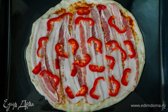 Затем на пиццу выложить полоски бекона и нарезанный красный болгарский перец. Посолить сверху.