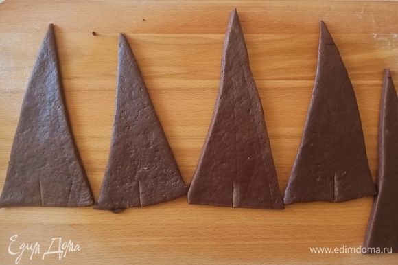 Раскатать тесто толщиной 0,5 см. Вырезать треугольники и каждый слегка растянуть в длину. У основания треугольника сделать небольшой надрез (1–2 см).