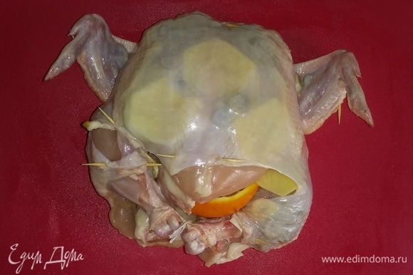 Затем внутрь куриной тушки положить апельсин и репчатый лук. Закрепить кожу тушки зубочистками, а ножки связать кулинарной нитью, чтобы начинка не выпадала.