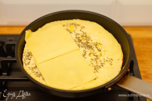 Когда омлет схватится, положить на одну сторону 2 пластинки плавленого сыра. Накрыть второй стороной омлета и жарить еще пару минут.