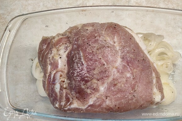 Духовку разогреть до 220°C. Развернуть мясо из пленки. На дно формы, в которой будет запекаться мясо, выложить весь лук, а сверху положить свинину. Запекать 15 минут. Потом уменьшить температуру до 200°C и запекать еще 35 минут.