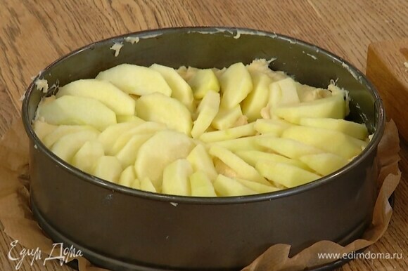 Дно разъемной формы выстелить бумагой для выпечки, выложить тесто и равномерно распределить, сверху веером разложить оставшиеся яблоки и посыпать сахаром.