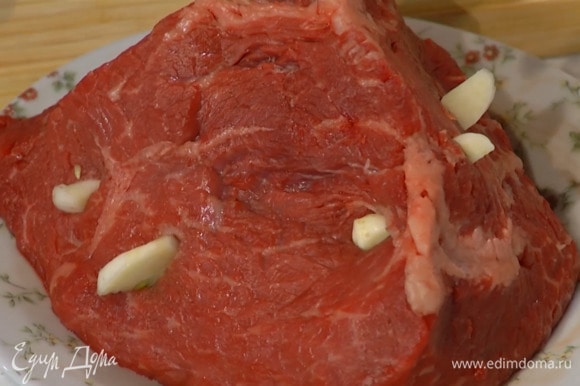 По всей поверхности мяса сделать кончиком ножа надрезы и вставить в них часть чеснока.
