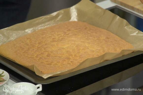 Влить тесто в выстеленный пекарской бумагой противень, равномерно распределить и выпекать в разогретой духовке 8 минут.