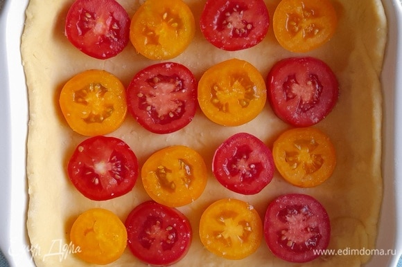 На тесто выложить часть кружков помидоров, чередуя по цвету.