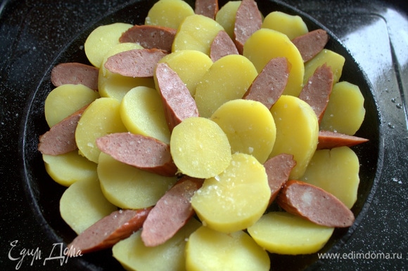 В той сковороде (22 см в диаметре), где жарился бекон, расположить ломтики картофели и между ними колбаску.