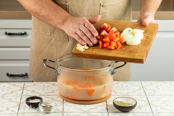Далее разрежьте на четвертинки лук, болгарский перец и помидоры, а зубчики чеснока раздавите ножом. Выложите в кастрюлю и оставьте вариться еще на 15 минут.