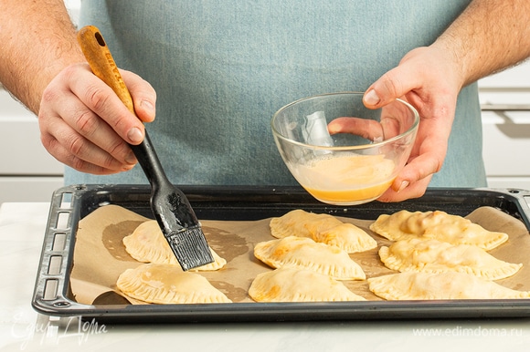 Противень застелите бумагой для выпечки, выложите пирожки. Яичный желток смешайте с 1 ст. л. молока и смажьте этой смесью заготовки.